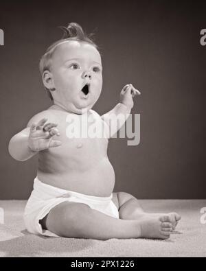 1960s CHUBBY BABY SITTING UP ARMS RAISED LOOK OF SURPRISE FACIAL EXPRESSION MOUTH AND EYES OPEN WIDE - b22453 HAR001 HARS JOY LIFESTYLE SOUND STUDIO SHOT HEALTHINESS HOME LIFE COPY SPACE FULL-LENGTH CLOTH CUTOUT SING DIAPER EXPRESSIONS AMAZED B&W WIDE YARN BUG-EYED AWE HUMOROUS DISCOVERY EXCITEMENT COMICAL DIAPERS UP CONCEPTUAL COMEDY OPEN-MOUTHED WIDE-EYED GROWTH JUVENILES OH STARTLED AMAZEMENT BABY GIRL BLACK AND WHITE CAUCASIAN ETHNICITY HAR001 MOUTH OPEN OLD FASHIONED Stock Photo