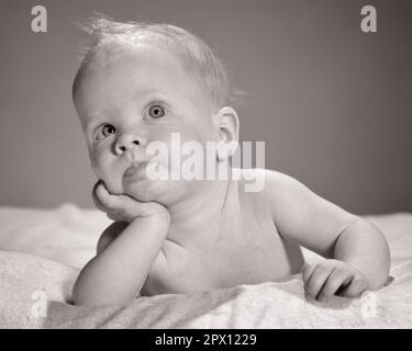 1960s WINSOME BRIGHT-EYED BABY GIRL LYING LEANING RESTING CHIN IN HAND LOOKING UP - b8155 HAR001 HARS EXPRESSIONS B&W DREAMS HEAD AND SHOULDERS STRATEGY DIRECTION ON UP CONCEPTUAL ALERT IMAGINATION STYLISH GROWTH IN HAND JUVENILES WONDERING BABY GIRL BLACK AND WHITE CAUCASIAN ETHNICITY HAR001 OLD FASHIONED PERPLEXED WINSOME Stock Photo