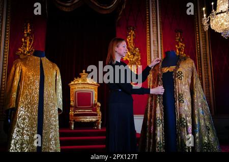 Caroline de Guitaut, deputy surveyor of the King's Works of Art for the Royal Collection Trust, adjusts the Imperial Mantle, which forms part of the Coronation Vestments, displayed in the Throne Room at Buckingham Palace, London. The vestments will be worn by King Charles III during his coronation at Westminster Abbey on May 6. Picture date: Wednesday April 26, 2023. Stock Photo