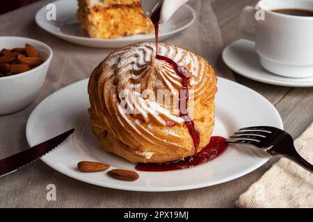 Almond profiterole cake on a plate with coffee. Sweet delicious dessert with berry syrup. Stock Photo