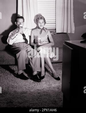 1950s COUPLE SITTING ON SOFA DRINKING BEERS WATCHING TELEVISION - f3164 HAR001 HARS FEMALES MARRIED SPOUSE HUSBANDS HOME LIFE COPY SPACE FRIENDSHIP FULL-LENGTH LADIES PERSONS MALES ENTERTAINMENT B&W PARTNER TELEVISIONS BEVERAGE BROADCASTING LEISURE FLUID CONNECTION BEERS STYLISH BREWSKI CHANNELS COOPERATION MID-ADULT MID-ADULT MAN MID-ADULT WOMAN RELAXATION TOGETHERNESS WIVES BEVERAGES BLACK AND WHITE CAUCASIAN ETHNICITY HAR001 OLD FASHIONED Stock Photo