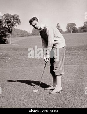 1920s MAN GOLFER ON PUTTING GREEN LOOKING AT CAMERA WEARING SWEATER PLUS FOURS AND TWO TONE SPECTATOR BROGUE STYLE GOLFING SHOES - g3644 HAR001 HARS SATISFACTION COPY SPACE FULL-LENGTH PERSONS MALES GOLFING ATHLETIC CONFIDENCE B&W EYE CONTACT ACTIVITY PHYSICAL WELLNESS ADVENTURE GOLFERS LEISURE STRENGTH STYLES AND CHOICE EXCITEMENT RECREATION HANDSOME ON CONNECTION FLEXIBILITY LINKS MUSCLES SPECTATOR STYLISH PLUS FOURS TWO-TONE FASHIONS FOCUSED MID-ADULT MID-ADULT MAN PRECISION YOUNG ADULT MAN BLACK AND WHITE CAUCASIAN ETHNICITY CONCENTRATING HAR001 OLD FASHIONED Stock Photo