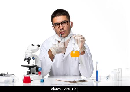 front view male doctor in white medical suit and with mask working with solution thinking on white background health pandemic covid virus coronavirus Stock Photo