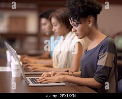 Studying diligently on her laptop. a young student working on her laptop with other students in the background. Stock Photo