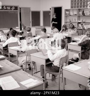 1960s TEACHER STANDING IN DOORWAY TO CLASSROOM MONITORING STUDENTS READING AND STUDYING AT THEIR DESKS - s15909 HAR001 HARS COPY SPACE HALF-LENGTH LADIES PERSONS MALES MIDDLE-AGED B&W DESKS SCHOOLS GRADE MIDDLE-AGED WOMAN HIGH ANGLE AFRICAN-AMERICANS AFRICAN-AMERICAN AND INSTRUCTOR BLACK ETHNICITY REAR VIEW OCCUPATIONS PRIMARY FROM BEHIND EDUCATOR MONITORING BACK VIEW EDUCATING EDUCATORS GRADE SCHOOL INSTRUCTORS MID-ADULT MID-ADULT WOMAN SCHOOL TEACHES BLACK AND WHITE CAUCASIAN ETHNICITY HAR001 OLD FASHIONED AFRICAN AMERICANS Stock Photo