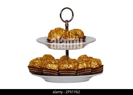 Pastries, desserts and sweets. Chocolate candies wrapped in golden foil on a two-storey etagere isolated on a white background. Clipping path. Decorat Stock Photo