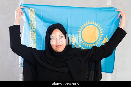 Happy young woman dressed in traditional islamic clothes with kazakh flag Stock Photo