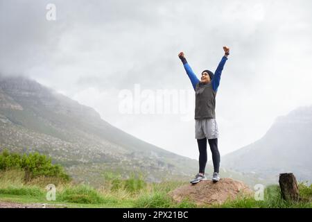 Feeling fit and free. A young man celebrating at the top of a mountain after reachin. Stock Photo