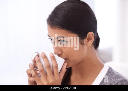 Enjoying some freshly brewed. A beautiful young woman enjoying a cup of coffee in her living room. Stock Photo