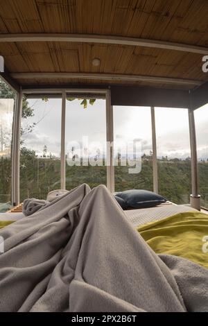 lifestyle, bedroom interior with a bed with blankets and large windows with plants in the background, scene of touristic place for vacation, nature Stock Photo