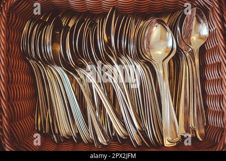 Close up shot of a stack of shiny metal spoons in a basket. Stock Photo