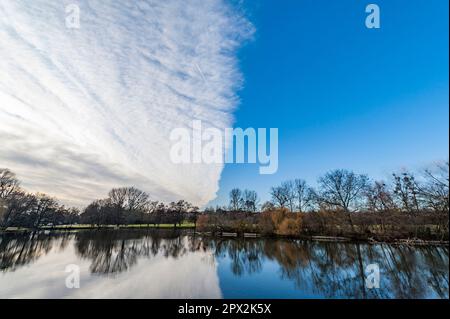 Looming veil clouds begin to cover the blue evening sky, dividing the image in half and reflecting in a lake Stock Photo