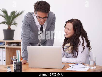 Working on the project as a team. Two businesspeople working on a laptop in their office. Stock Photo