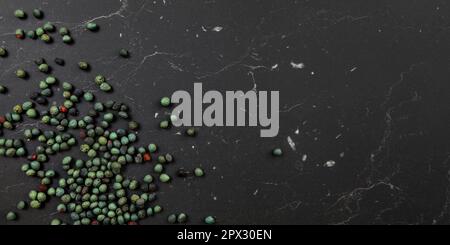 Tabletop view, Black pepper (Piper nigrum) spice spilled on dark marble like board. Turkish green / blue peppercorn variant. Banner with space for tex Stock Photo
