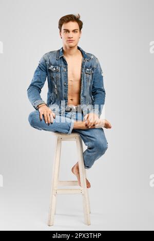 Young man in denim clothes sits on tall chair Stock Photo