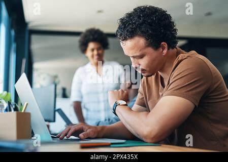 Is it 5pm yet. a young businessman using a latop while checking the time in an office Stock Photo