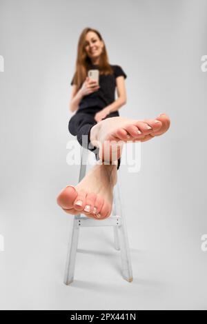 Young woman pulling her barefoot legs forward and making photo with her mobile phone (focus on foreground) Stock Photo