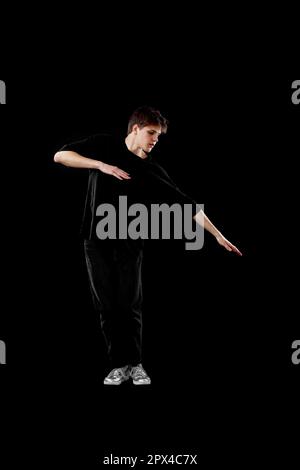 young man in black t-shirt dancing on black background. Full length Stock Photo