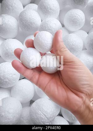 Hand holding white polystyrene foam beads ball drop from Styrofoam machine for fragile stuff packaging box on blue modern luxury background for decora Stock Photo