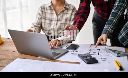 Close-up image of a professional engineer team are working together in the office, checking building plan on laptop and blueprint. Stock Photo