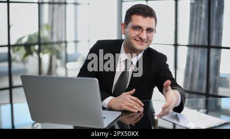 working at the computer, makes an inviting gesture, offers to sit down for an interview Stock Photo