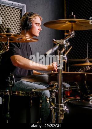 Young man wearing headphones and playing drums in a recording studio. Stock Photo