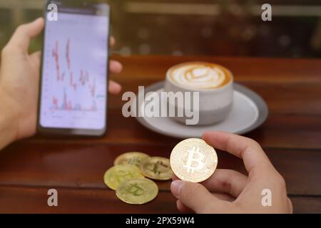 Close up of male hand holding bitcoin and mobile phone with candlestick chart on screen. Cryptocurrency trading concept Stock Photo