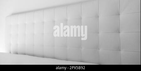 Soft headboard. Upholstery for furniture made of genuine or artificial leather and quilted fabric. Soft headboard against a light wall. Black and whit Stock Photo