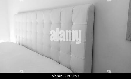 Soft headboard. Upholstery for furniture made of genuine or artificial leather and quilted fabric. Soft headboard against a light wall. Black and whit Stock Photo