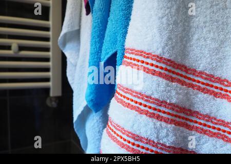 Towels hang next to a heated towel rail, wall radiator or radiator. White, blue, pink, red towels. Organization of household items in the bathroom. Ho Stock Photo