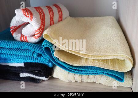 Towels on a shelf in a white cabinet. Clean ironed pink, yellow, blue towels folded in a pile. Organization of household items in the bathroom or clos Stock Photo