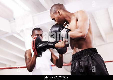 Improving on all aspects of his boxing. A boxer practicing with his sparring partner in the ring. Stock Photo
