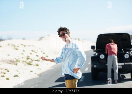 I guess well have to hitchhike. A young man trying to hitch a ride while his friend looks at the engine in the background. Stock Photo