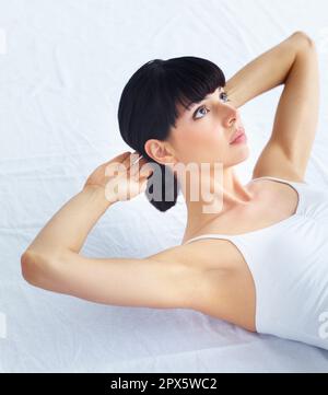 Building a well-defined tummy. Young fit woman doing sit-ups and looking away. Stock Photo