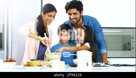 They proud their kids made pancakes for the first time. a young family making pancakes together in the kitchen at home Stock Photo