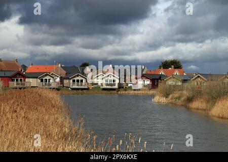 Under threating skies holiday lodges look quite bright around a reed fringed lake on the Bay holiday park near Filey in North Yorkshire. Stock Photo