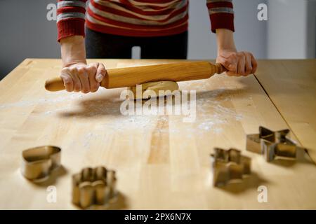 Unrecognizable woman rolls out ginger dough with rolling pin on kitchen table Stock Photo