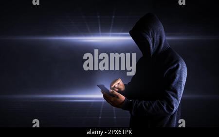 Hacker Using Smartphone. Men in black clothes with hidden face looks at smartphone Stock Photo