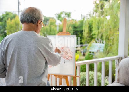 Lifestyle artist. Senior old man painting picture artwork using brush and water color on canvas, portrait elderly white haired paint at his easel outs Stock Photo