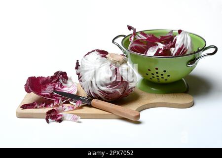Cicorino (Cichorium intybus var. foliosum) rosso on wooden board, cut with knife Stock Photo