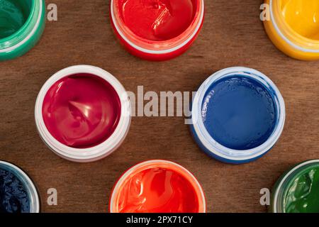 Gouache paints standing on wooden table, flat lay. Eight open jars of artistic gouache paint on horizontal surface, top view Stock Photo