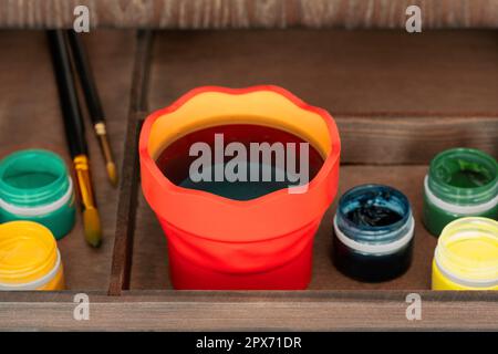 Paint cup for rinsing paintbrushes, open gouache bottles and paintbrushes in easel box, high angle shot Stock Photo