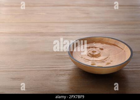 Drop falling down into bowl with clear water on wooden table. Space for text Stock Photo