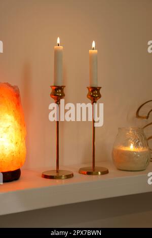 Pair of beautiful candlesticks, scented candle and salt lamp on white shelf Stock Photo