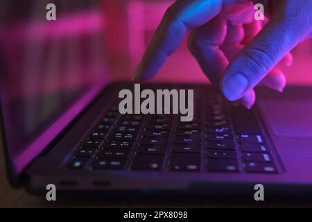 Person typing at laptop computer at night. Female uses keyboard, shakes buttons with fingers. Internet security, cyber attack. Trendy neon light. Crea Stock Photo