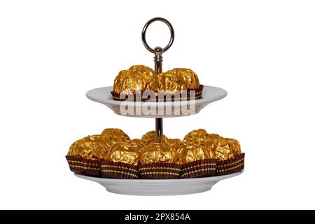 Pastries, desserts and sweets. Chocolate candies wrapped in golden foil on a two-storey etagere isolated on a white background. Clipping path. Decorat Stock Photo