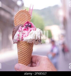 Hand holding colorful mixed italian ice cream in a fresh waffle. Close-up. Stock Photo