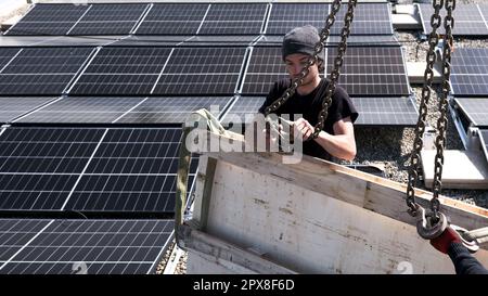 Male team engineers installing stand-alone solar photovoltaic panel system. Electricians mounting blue solar module on roof of company roof. Alternati Stock Photo