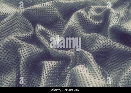 Synthetic fabric with holes laid in waves. Beautiful drape. Fabric for curtains, interior design, and decor. Wrinkled gray fabric Stock Photo