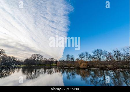 Looming veil clouds begin to cover the blue evening sky, dividing the image in half and reflecting in a lake Stock Photo